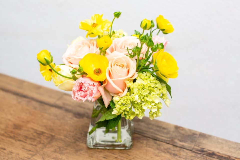 Butterfly ranunculus, roses, tulips & green hydrangeas in a clear vase.