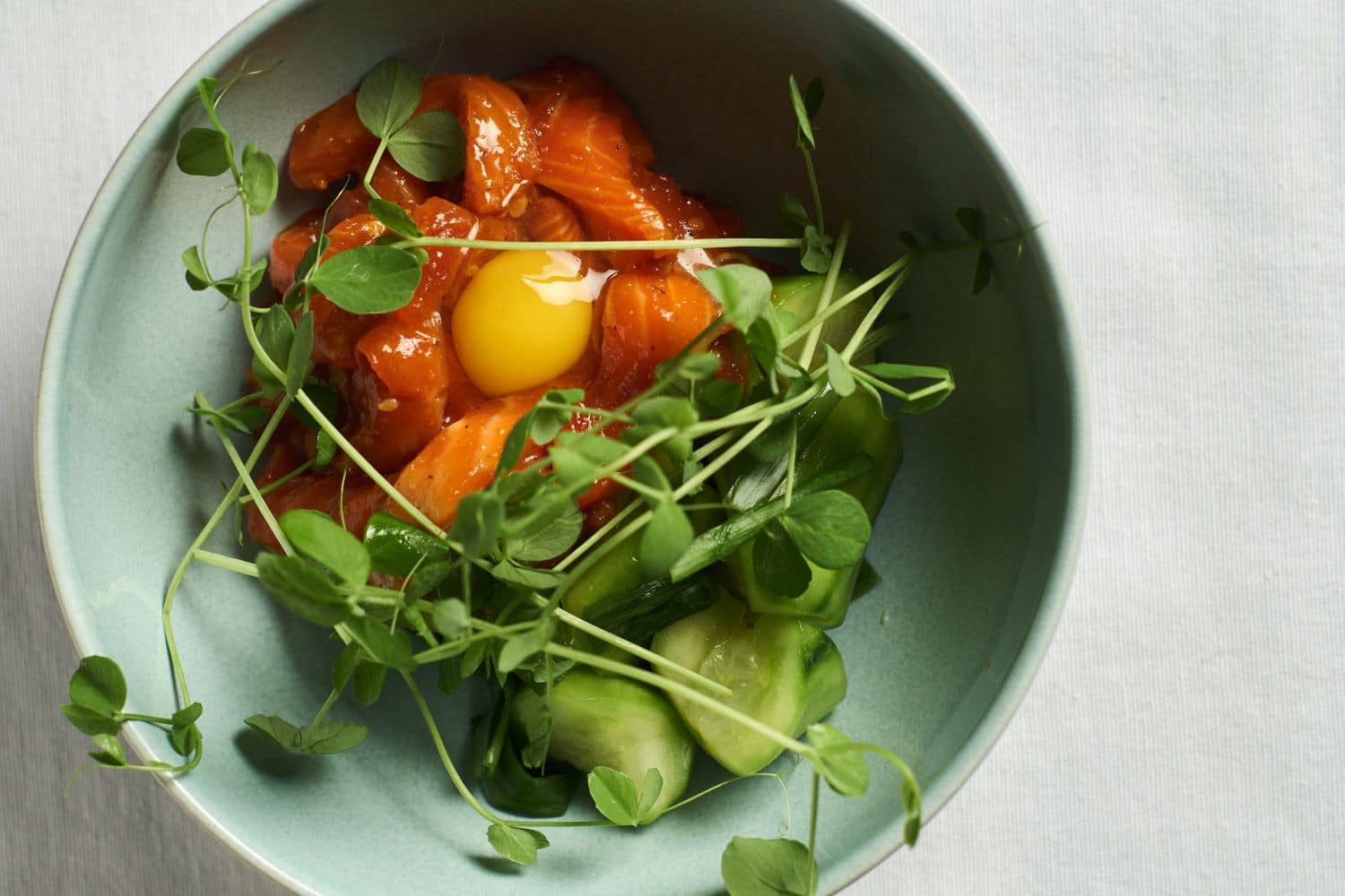 King Salmon sashimi over a bed of pickled cucumbers, micro greens and quail egg