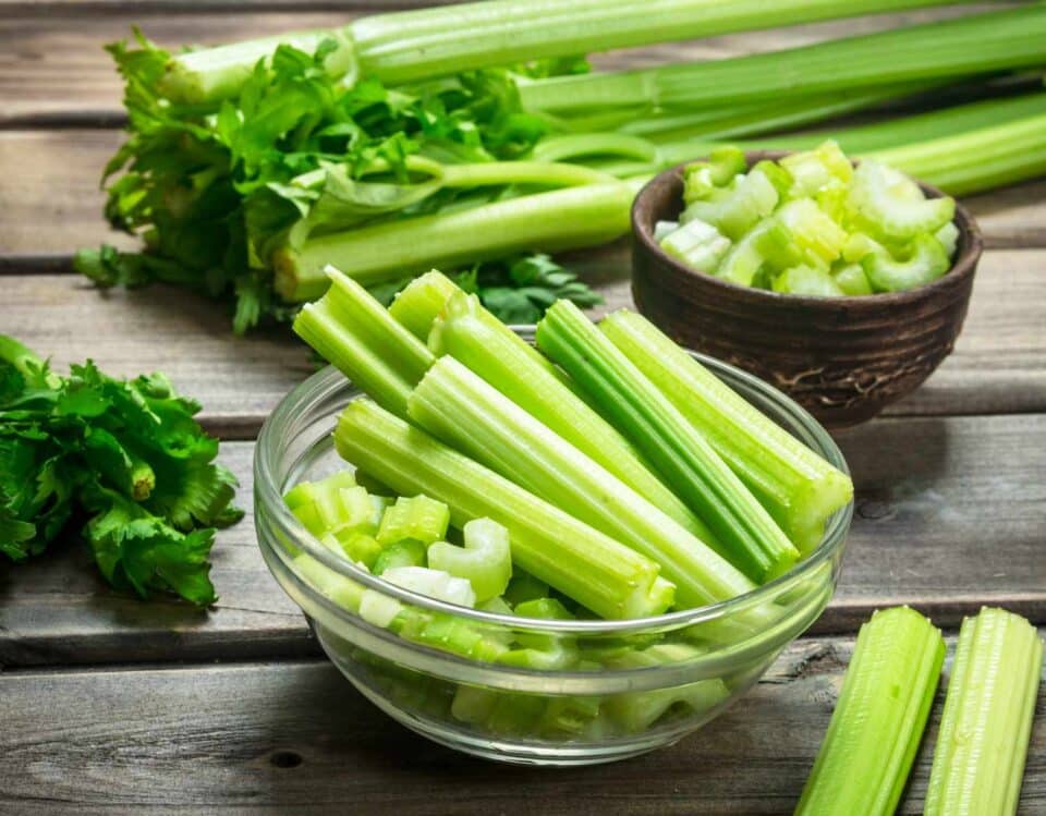 sliced and chopped celery in glass bowls on a wood table