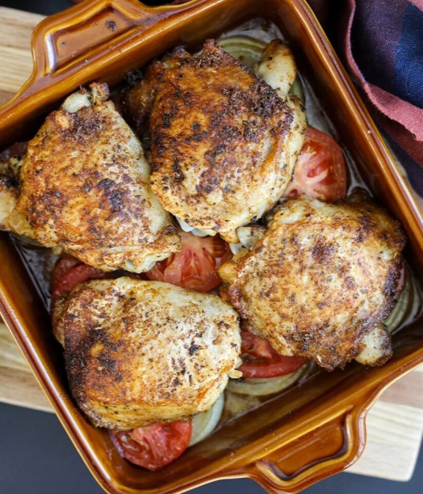 roasted chicken thighs on a bed of vegtables in a roasting pan