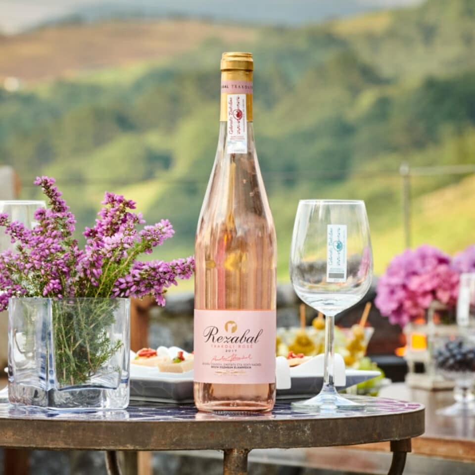 Rezabal Txakolina Rosé on a table outdoors with flowers and a wine glass